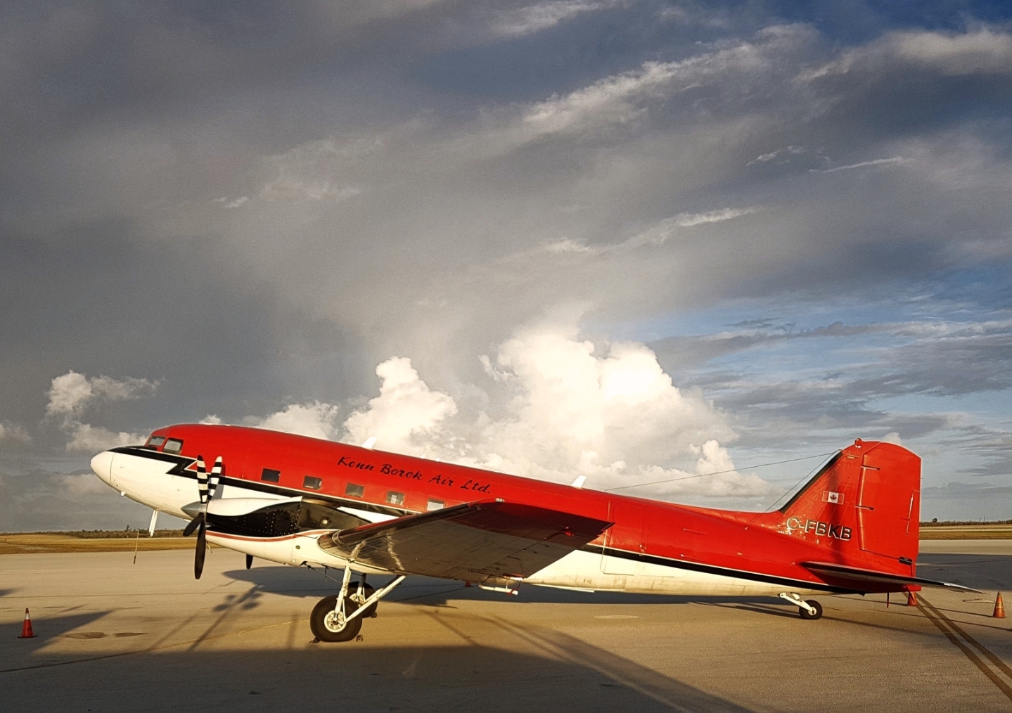 Photograph of a red-and-white twin-engine propeller aircraft marked “Kenn Borek Air Ltd.” and registration C-FBKB parked on a paved apron.