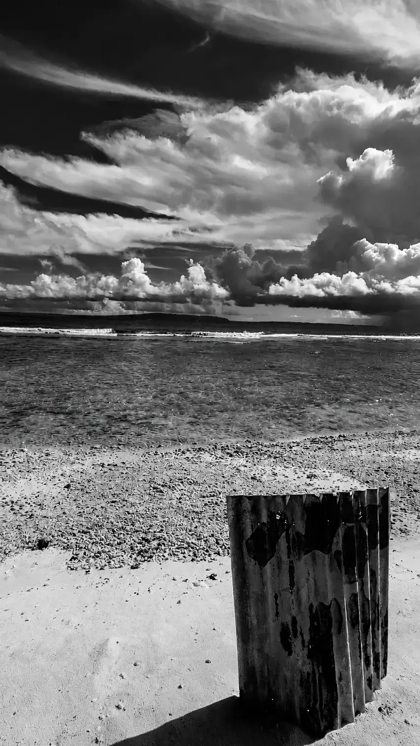 Weathered corrugated metal resting on a beach beneath dramatic clouds in the Mariana islands